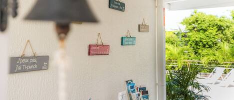 Una pared con letreros colgantes y una campana, una mesa con libros y una carta, y vista a zonas verdes al exterior.