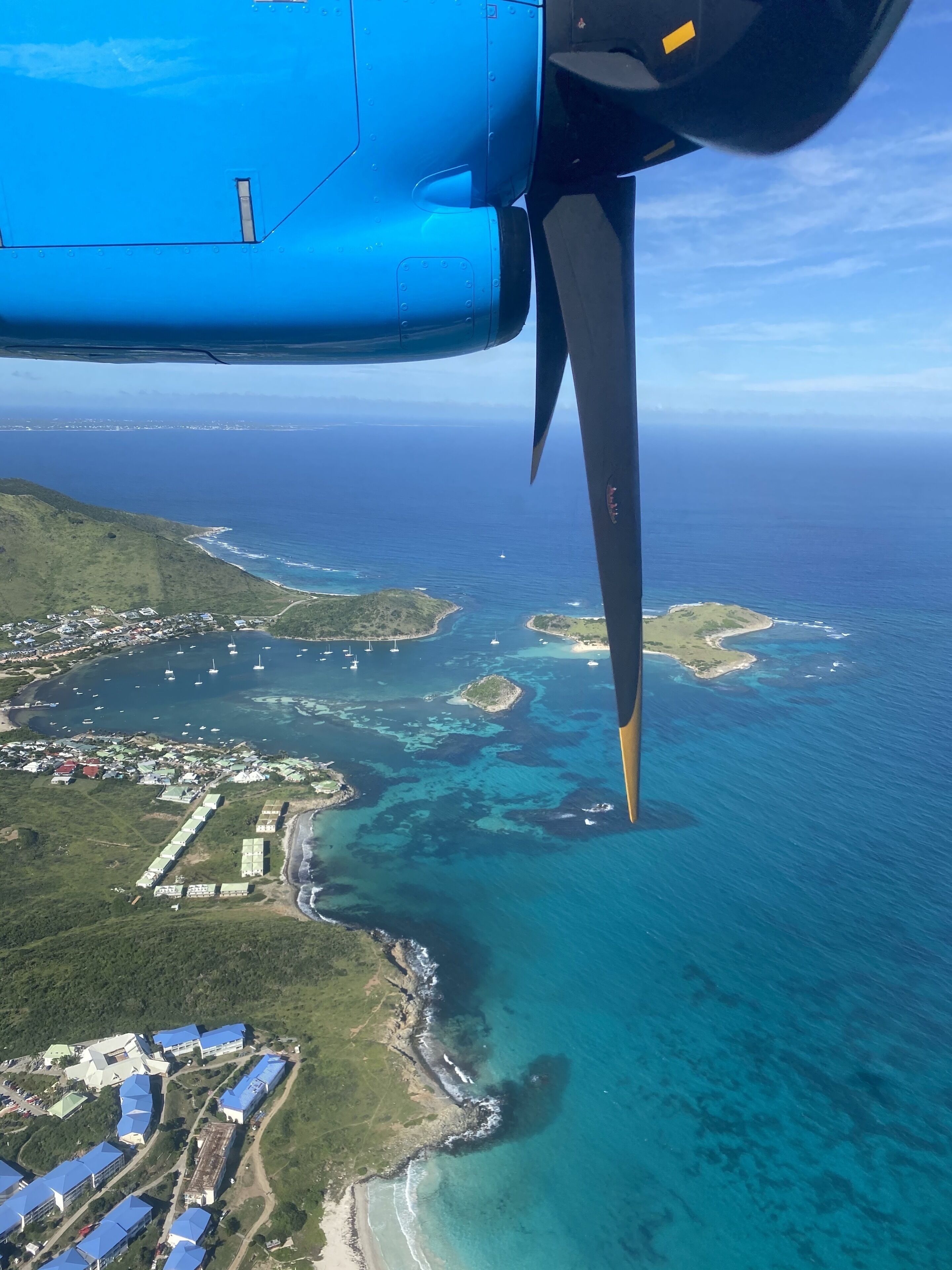 An aerial view of a coastal area with clear blue waters, green land, and a jet engine in the foreground.