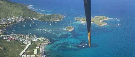 An aerial view of a coastal area with clear blue waters, green land, and a jet engine in the foreground.