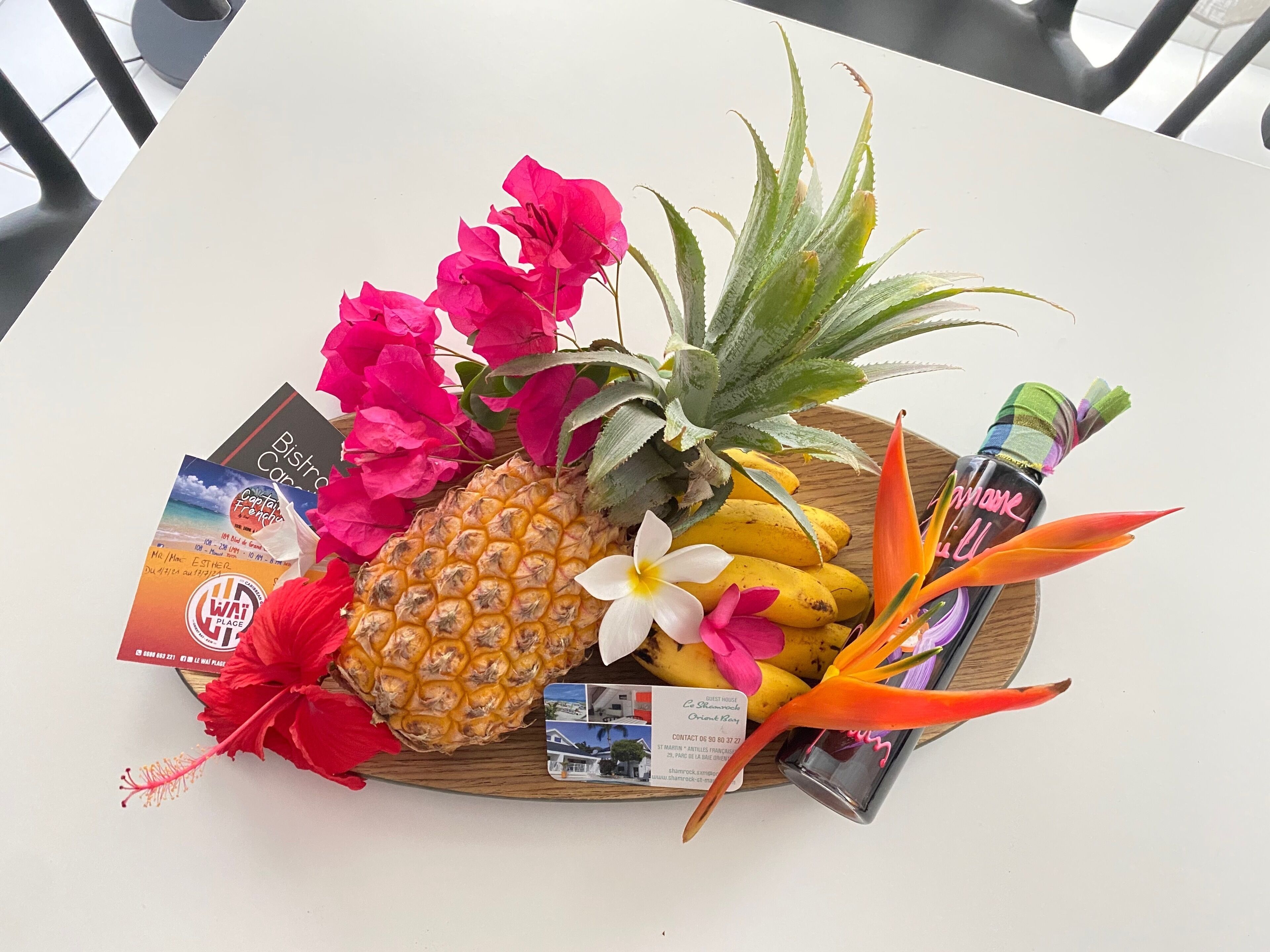 Un plateau en bois contenant un ananas, des bananes, une fleur d’hibiscus, des feuilles d’aloe vera et un flacon de parfum.