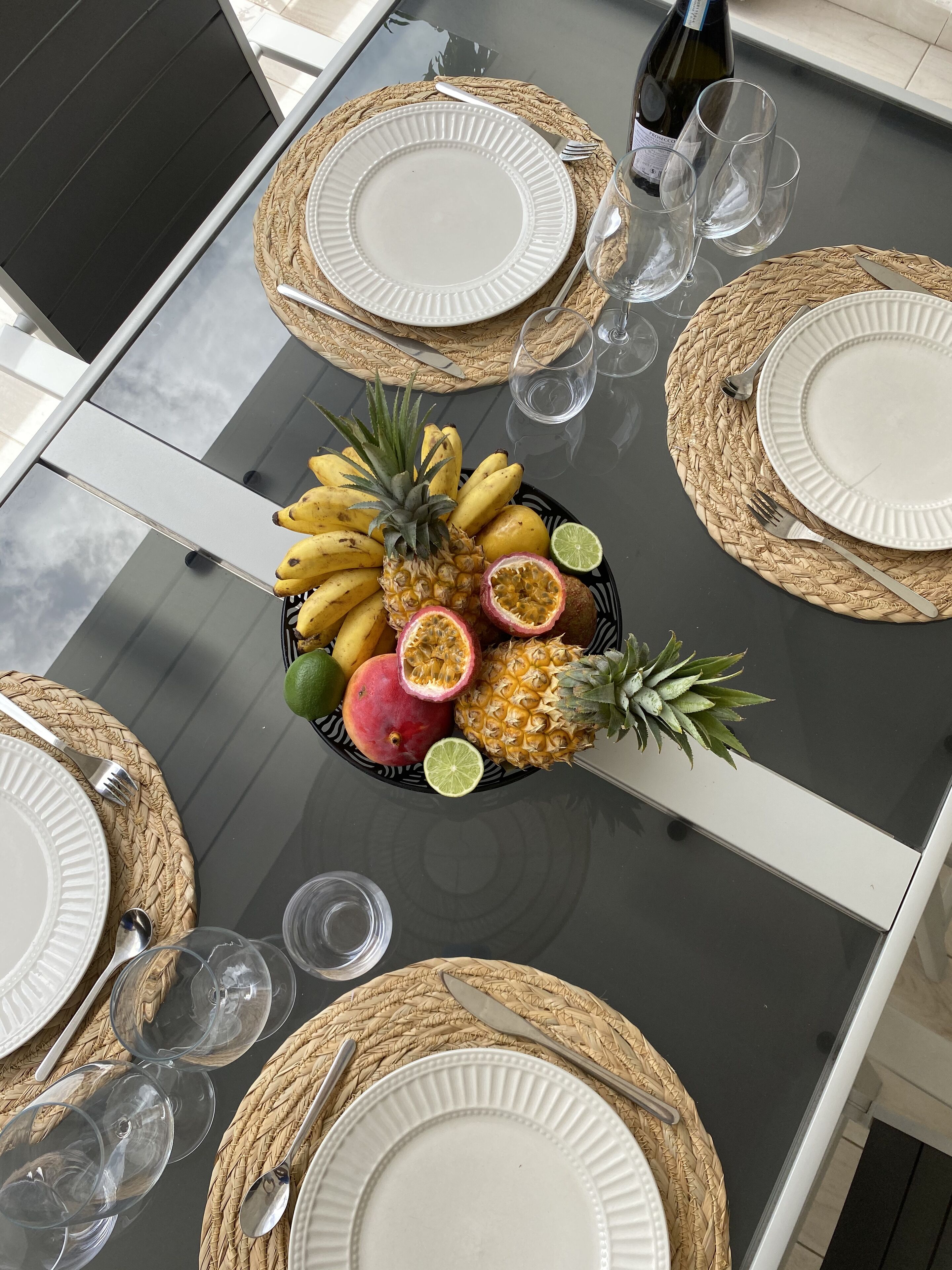 Mesa posta com pratos, talheres e uma peça central de frutas.