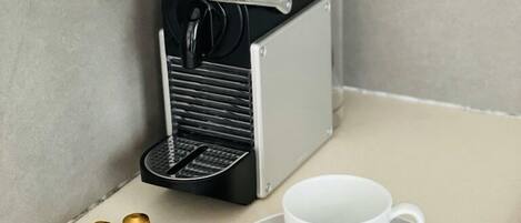 A small kitchenette with a coffee machine, a cup, and a spoon on a tray.