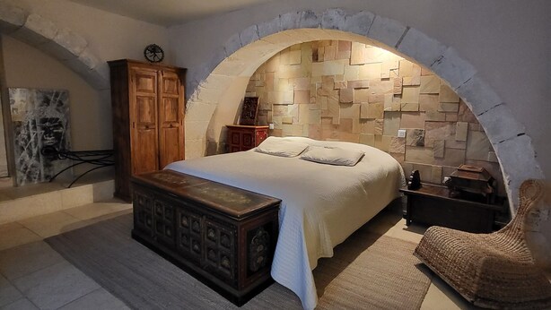 A bedroom with a stone archway, a bed with a white bedspread, a wooden chest of drawers, and a woven chair. - In a quiet location between Aix and Marseille. Provence. Beach 10 km away, with no buildings directly across from the property  (Lançon-Provence)