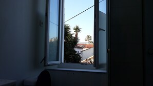 A room with a window overlooking a residential area, including a house with a red roof and palm trees. - Studio 15m2 seaside (La Seyne-sur-Mer)