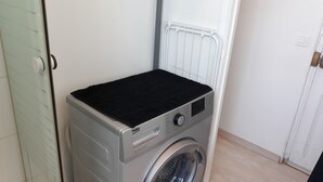 A compact, front-loading washing machine with a black top, located in a small laundry room with a white door and a white radiator. - Studio 15m2 seaside (La Seyne-sur-Mer)