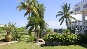 A tropical garden with palm trees and potted plants, a pool, and a two-story building with balconies. - Beautiful apartment on the west coast of Reunion Island - Promo 19/05 to 22/05 (Saint Paul)