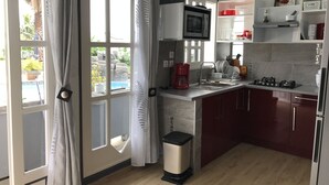 A modern kitchen with a built-in microwave, a sink, and a gas stove. There is a window with a view of a pool and greenery outside. - Beautiful apartment on the west coast of Reunion Island - Promo 19/05 to 22/05 (Saint Paul)