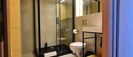 Uma casa de banho moderna com chuveiro separado por vidro, sanita e lavatório com espelho.