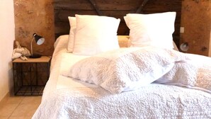 Ein Bett mit weißer Bettwäsche und Kissen, ein Nachttisch mit Lampe und eine rustikale Holzbalkendecke.