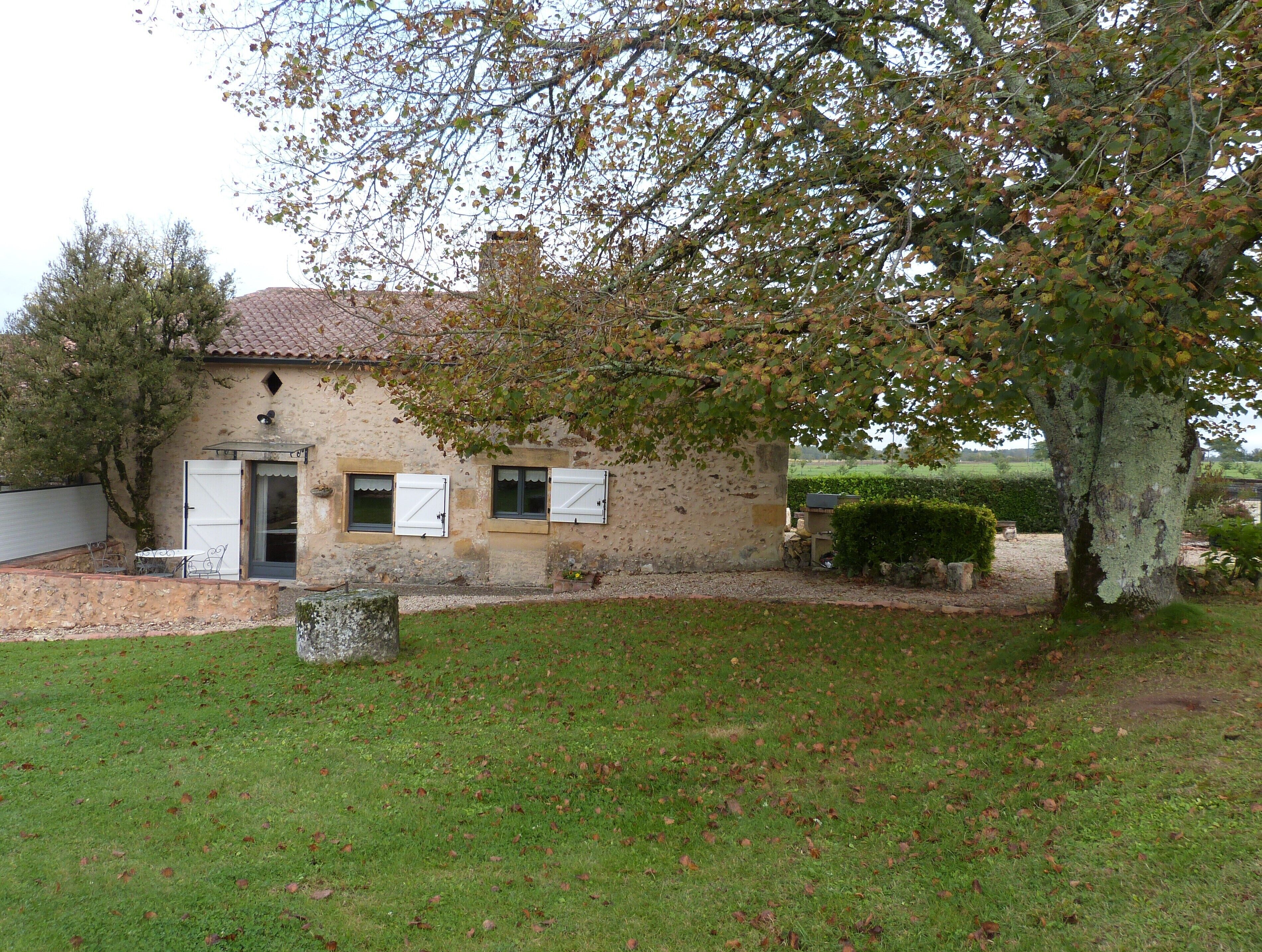 Une maison de campagne en pierre, avec un toit en tuiles, un petit porche à l’avant et une pelouse bien entretenue.