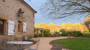 Ein rustikales Steinhaus mit einer Terrasse, auf der ein runder Tisch und Metallstühle stehen.