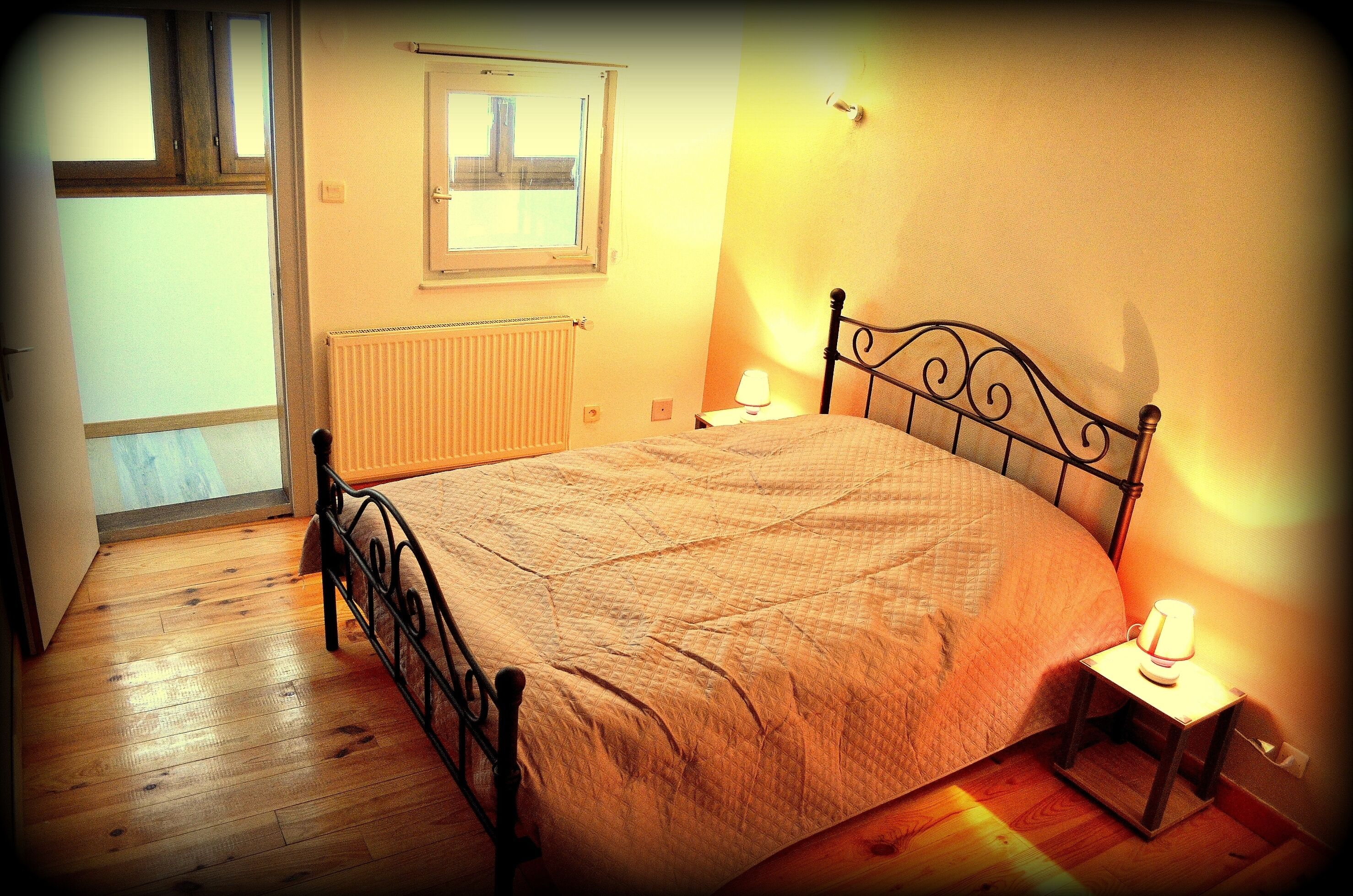 A bedroom with a bed, a nightstand, a window, and a radiator.