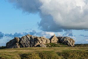 A stone house with a thatched roof, surrounded by large boulders and a grassy field.