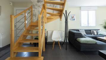 Un salon moderne avec un escalier en bois, un canapé noir et un radiateur blanc.