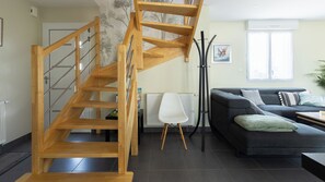 Un salon moderne avec un escalier en bois, un canapé noir et un radiateur blanc.