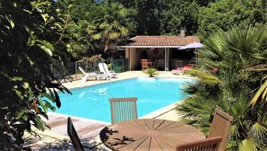 A backyard with a swimming pool, surrounded by lush greenery and a small patio area with chairs and a table. - Large luxury villa in the middle of the forest, heated swimming pool, quiet garden. (Capbreton)