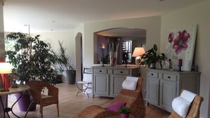 A spacious living area with wicker furniture, a dining table, and a kitchen in the background. - Large luxury villa in the middle of the forest, heated swimming pool, quiet garden. (Capbreton)