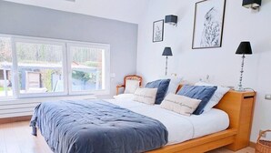 Une chambre à coucher avec un lit en bois, une literie blanche et bleue, une fenêtre donnant sur l’extérieur et des lampes fixées au mur.
