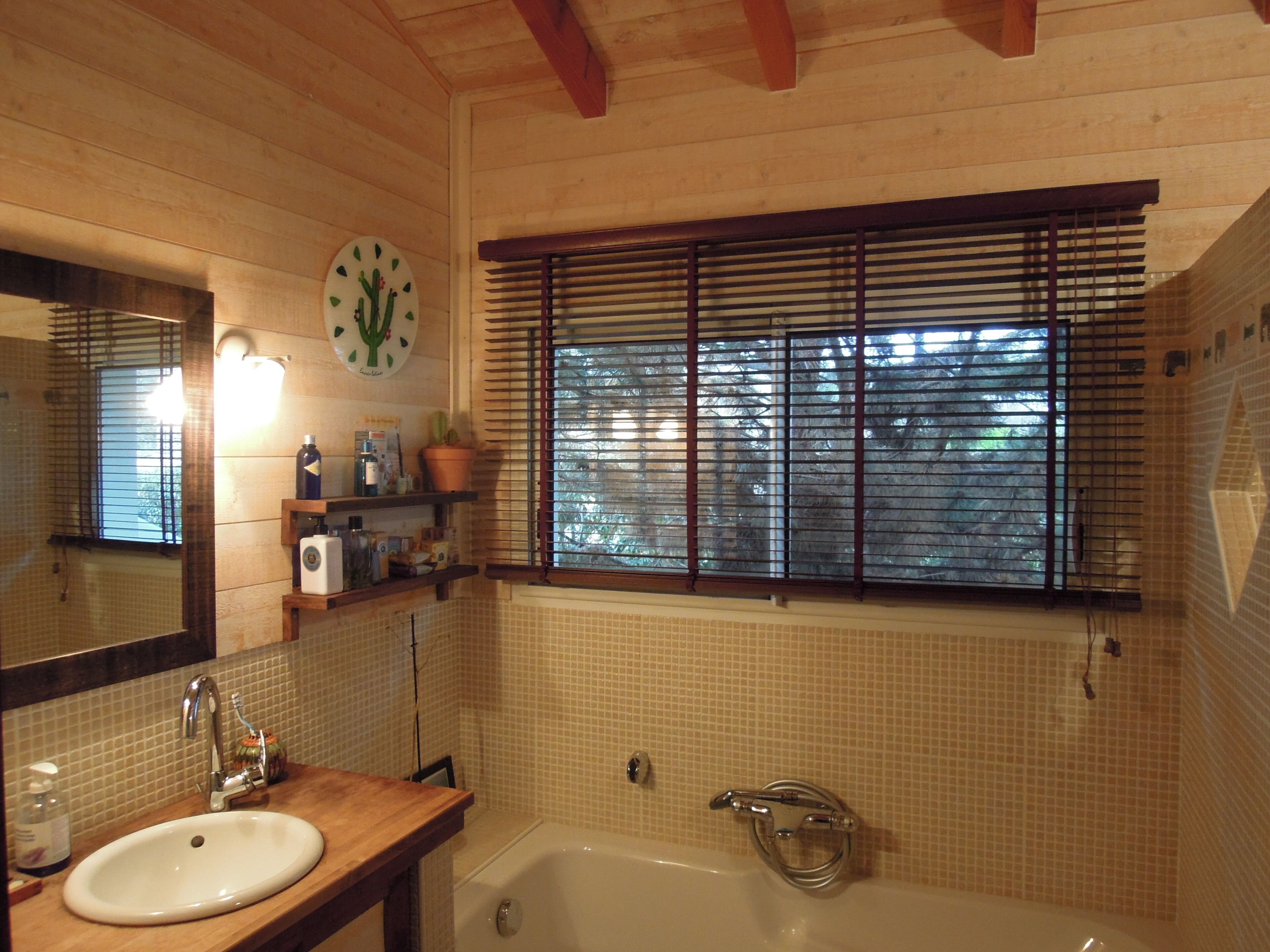 A bathroom with a wooden vanity, a sink, a bathtub, a window with blinds, and a wall clock.