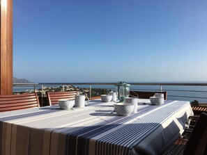 Mesa de comedor dispuesta con cuencos estampados y un farol en un balcón con vista al mar.