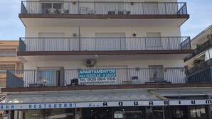 A multi-story building with balconies, a restaurant, and parked cars.