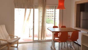 A dining area with a table and chairs, a hanging light fixture, a refrigerator, and a sliding glass door leading to an outdoor balcony.