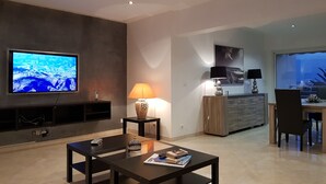 A modern living room with a flat-screen TV, a coffee table, a lamp, and a dining area with a view. - Apartment in front of the beach, superb sea view and terrace 🏖️🏖️🏖️ (Saint-Cyr-sur-Mer)