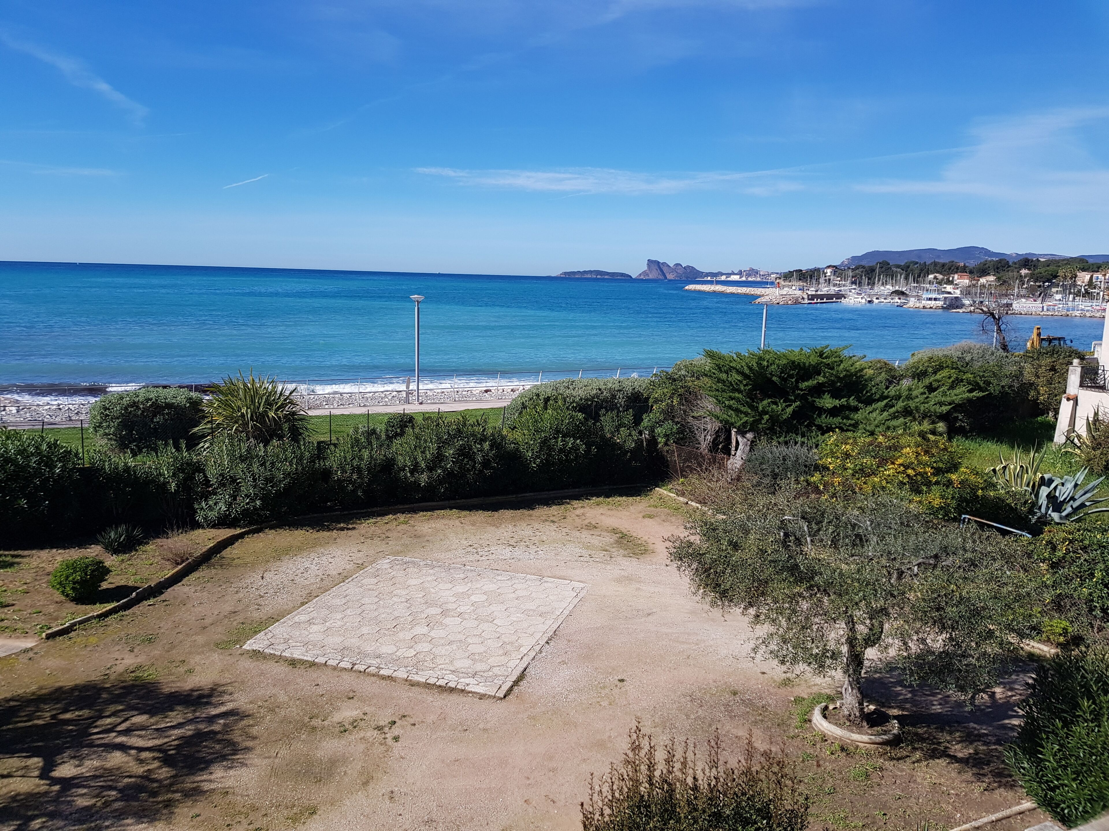 Une vue sur la côte, avec une zone pavée, de la végétation et une mer bleue et limpide.
