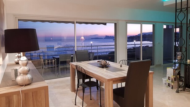 A dining area with a view of the sea at sunset, a table with chairs, and a lamp. - Apartment in front of the beach, superb sea view and terrace 🏖️🏖️🏖️ (Saint-Cyr-sur-Mer)