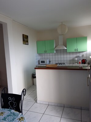 A kitchen with green cabinets, a microwave, a gas stove, and a coffee maker. - ALL COMFORT and BRIGHT, first floor of a villa, BALCONY, VIEW of the Caribbean SEA (Schoelcher)