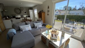 Een moderne woonkamer met een grijze bank, een bijzettafeltje met decoratieve objecten, en een uitzicht op de achtertuin door een schuifdeur van glas.