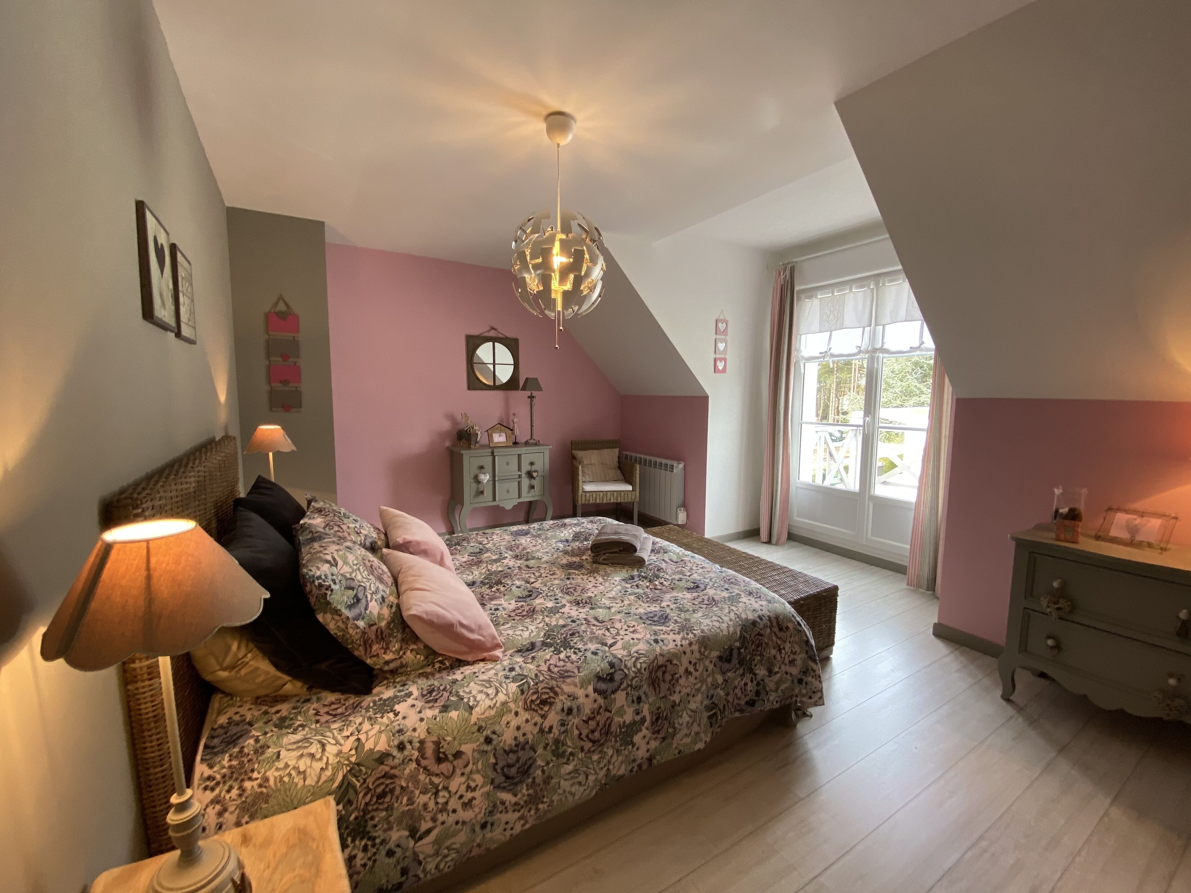 A bedroom with a bed, a dresser, a lamp, a ceiling fan, and a window with curtains.