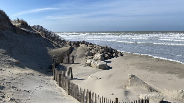 Een zandstrand met een houten omheining en grote rotsen.