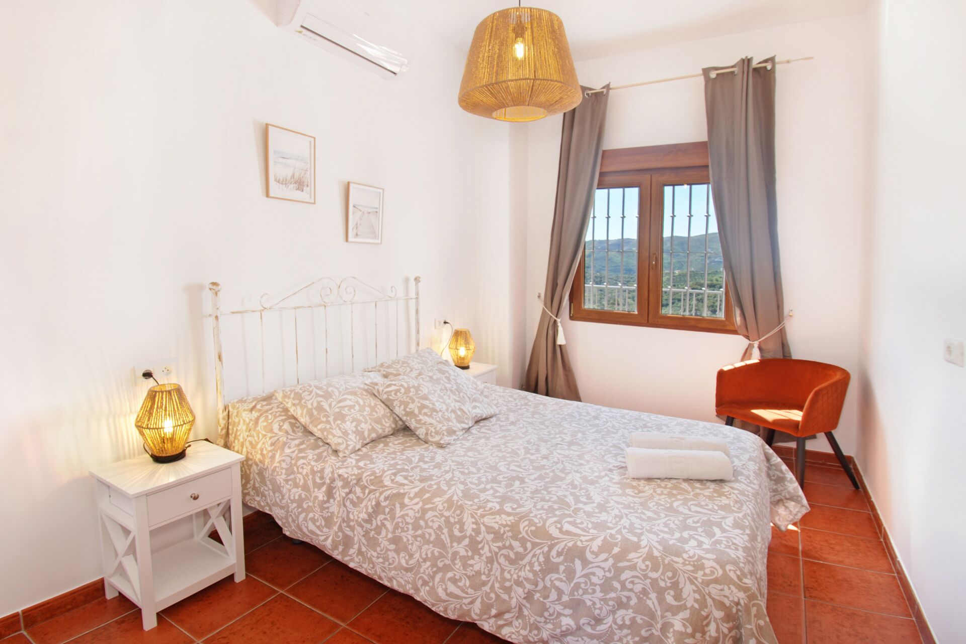 A bedroom with a bed, bedside lamps, a window with curtains, a chair, and a view of the outdoors.