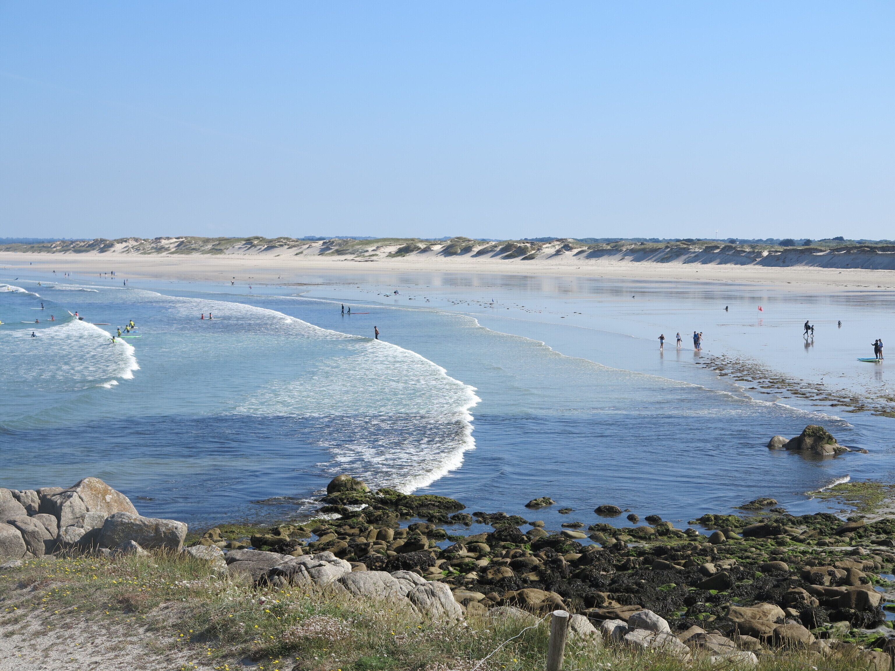 Een strand met helder water, een rotsachtige kustlijn en mensen in het water.