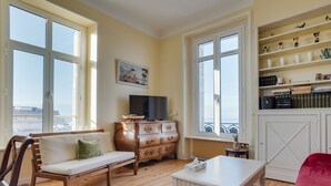 A living room with a sofa, a coffee table, a TV, a bookshelf, and a view through large windows. - Apartment for 5 in Arcachon with secure parking (Arcachon)