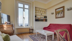 A living room with a white sofa, a red sofa, a coffee table, a TV on a wooden cabinet, a bookshelf, and a window with a view. - Apartment for 5 in Arcachon with secure parking (Arcachon)