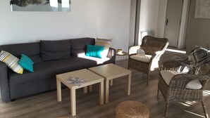 A modern living room with a grey sofa, teal cushions, wicker chairs, and a wooden coffee table. - Villa Trémière - Sea view and 28 ° C heated swimming pool (Cavalaire-Sur-Mer)