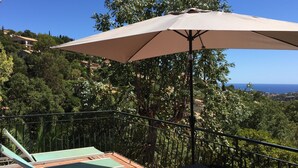 A terrace with a large umbrella, two lounge chairs, and a view of the sea and hills. - Villa Trémière - Sea view and 28 ° C heated swimming pool (Cavalaire-Sur-Mer)