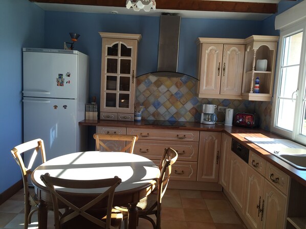 A kitchen with wooden cabinets, a refrigerator, a dining table with chairs, and a window. - COTENTIN, SEASIDE, NICE INDEPENDENT COUNTRY CLASS 4 STARS 8 PEOPLE (Réville)