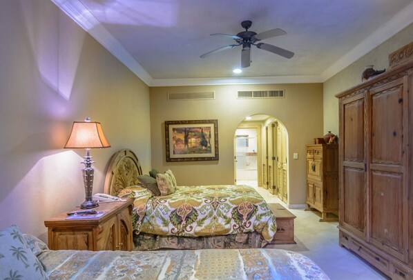 A bedroom with a bed, a nightstand, a lamp, a ceiling fan, a painting, and wooden cabinets.