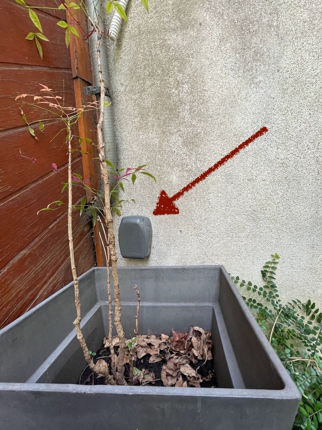 A gray planter box with a red arrow pointing to a gray object on the wall.