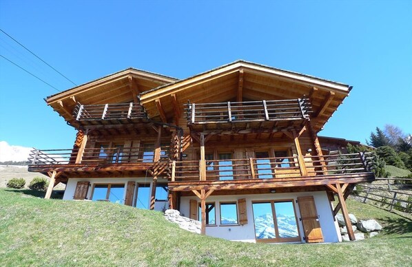 Un chalet en bois à deux étages, doté de balcons, de grandes fenêtres et surplombant un paysage montagneux.