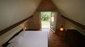 Une chambre avec un plancher en bois, un lit avec une literie blanche, une commode et une porte donnant sur l’extérieur.
