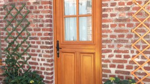 Puerta de madera con un panel de vidrio, flanqueada por paredes de ladrillo y macetas con plantas.