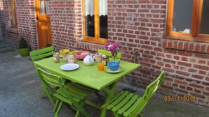 Mesa verde dispuesta con alimentos para el desayuno, una planta en maceta y una ventana con vista a un edificio de ladrillo.