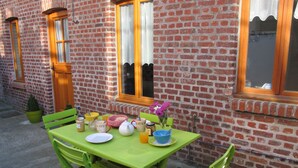 Mesa verde dispuesta con alimentos para el desayuno, una planta en maceta y una ventana con vista a un edificio de ladrillo.