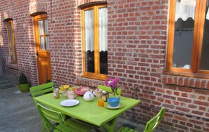 Ein grüner Tisch, gedeckt mit Frühstücksgebäck, eine Topfpflanze und ein Fenster mit Blick auf ein Ziegelgebäude.