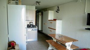 A compact kitchen with a refrigerator, a coffee maker, and wooden cabinets. - Apartment at the foot of the Arc 2000 slopes (BOURG SAINT MAURICE)