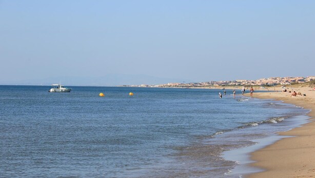 Ein Strand mit ruhigem Wasser, einem Boot und Menschen, die das Ufer genießen.